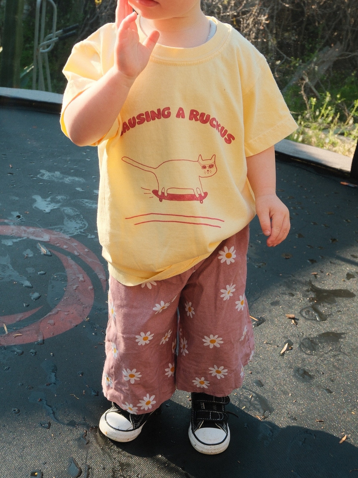 Child wearing a yellow shirt with text and graphics, standing on a playground surface.