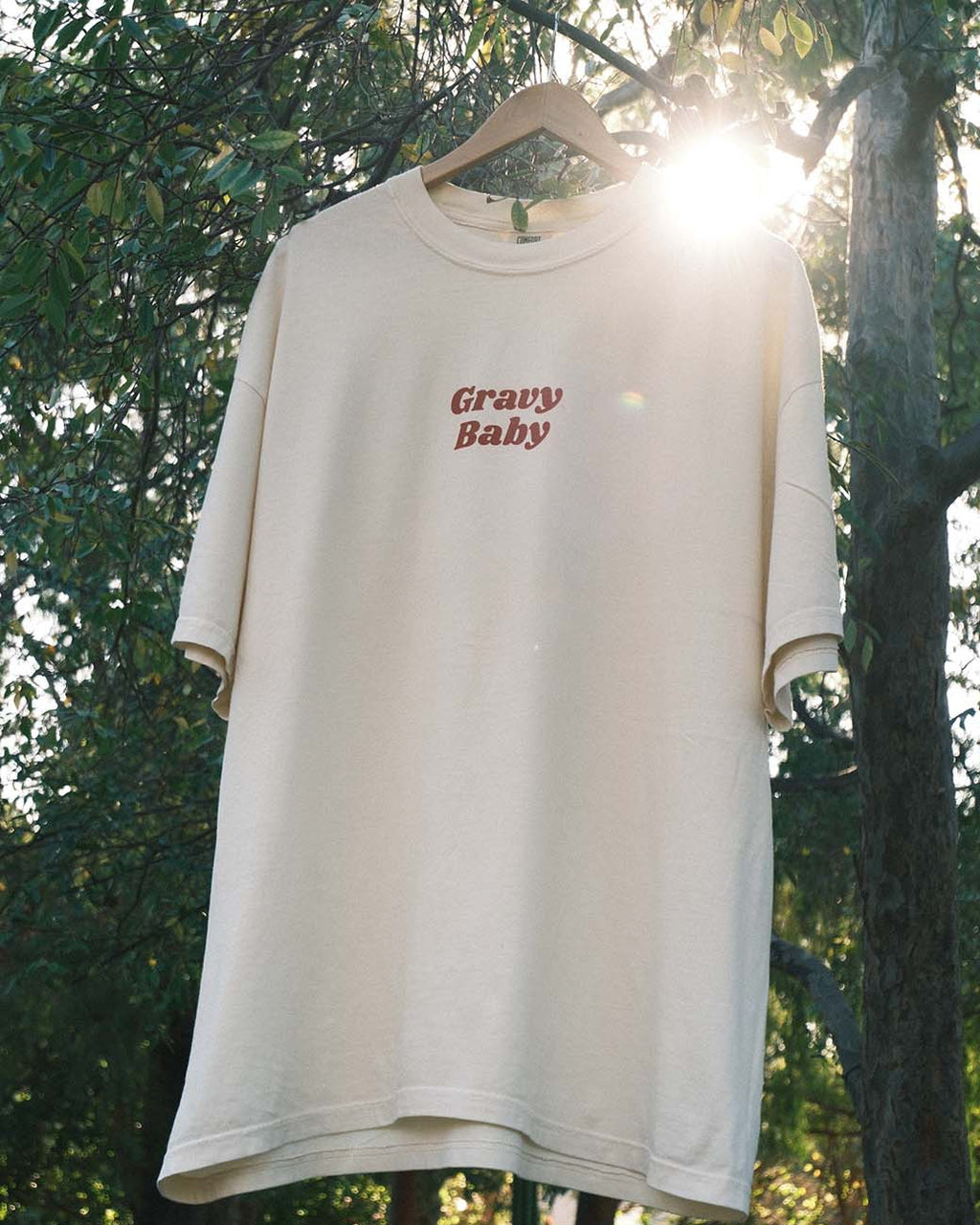 Beige oversized t-shirt with 'Gravy Baby' text on a hanger against a natural background.