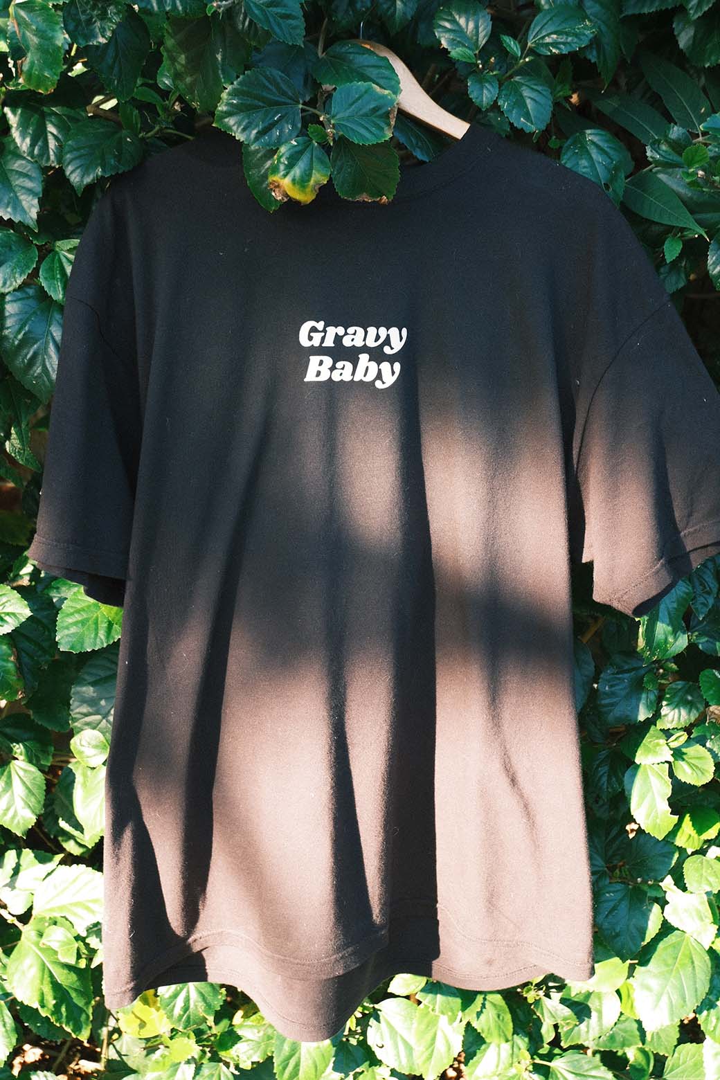 Black t-shirt with 'Gravy Baby' text hanging against a green leafy background