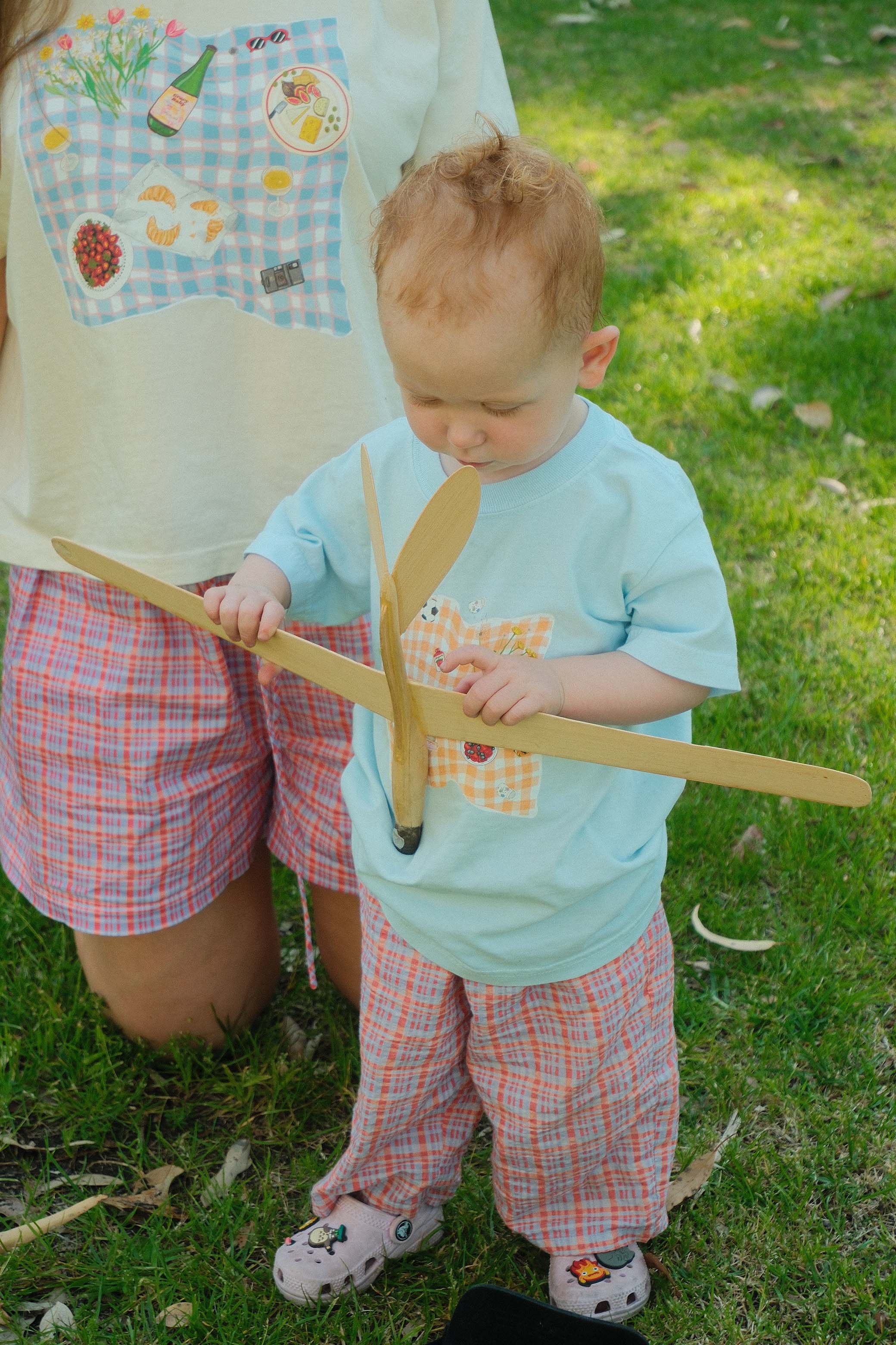Child holding a wooden plane outdoors on grass