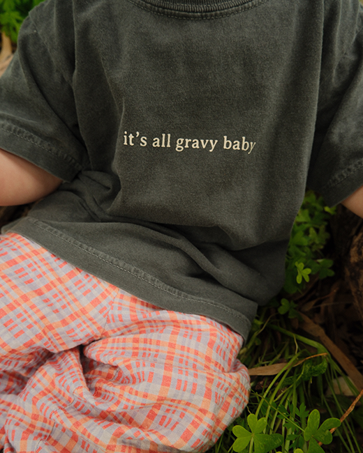 Person wearing a dark shirt with 'it's all gravy baby' text, sitting on grass.