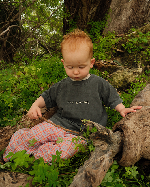 Child sitting on a log in a forest with text on shirt