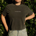 Person wearing a black t-shirt with 'it's all gravy baby' text in front of green foliage.