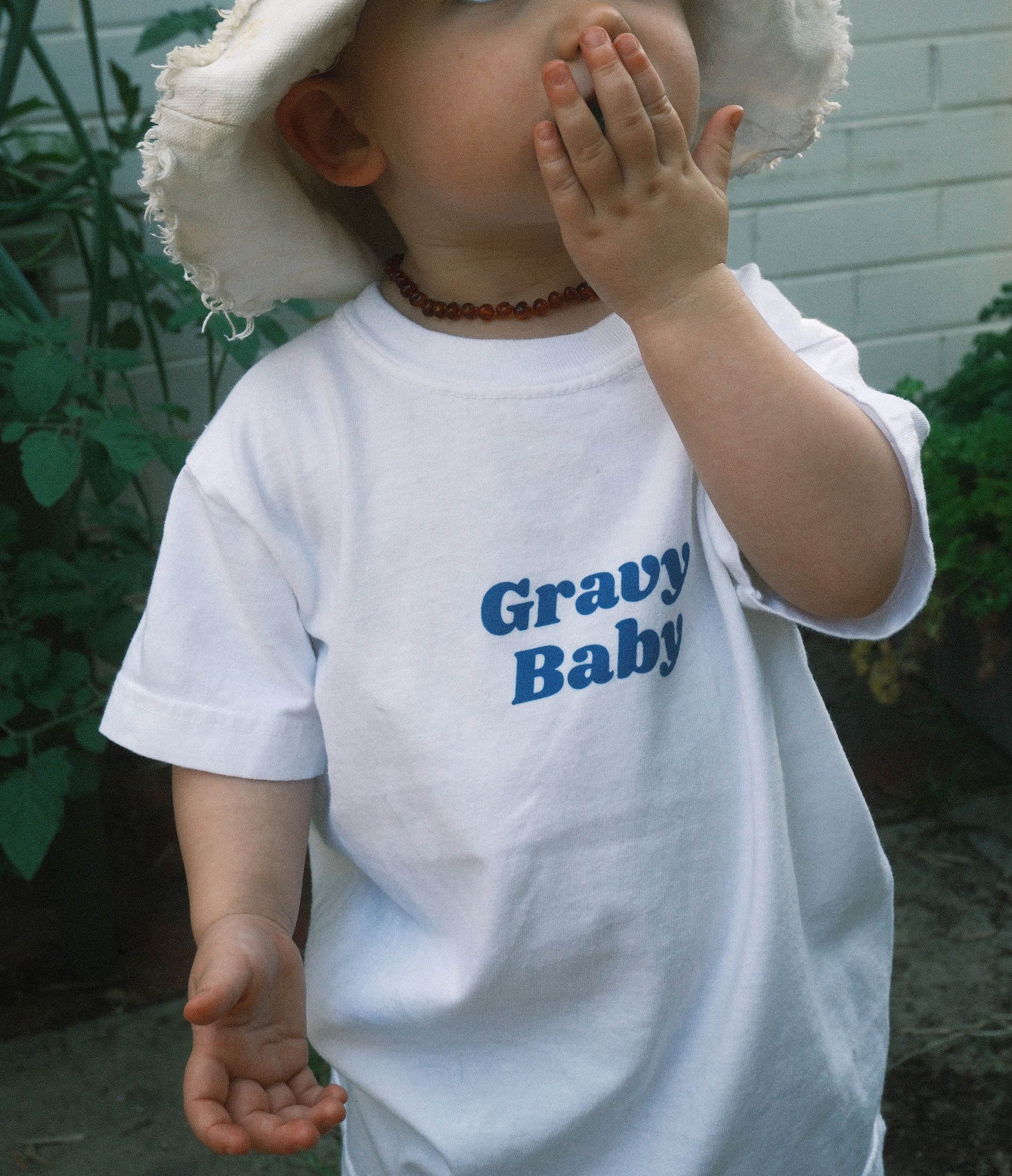 Child wearing a white t-shirt with 'Gravy Baby' text, outdoors.
